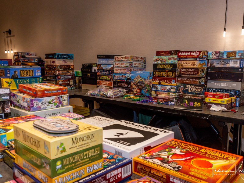 DSC_8750 A large collection of various board games stacked on tables in a room.